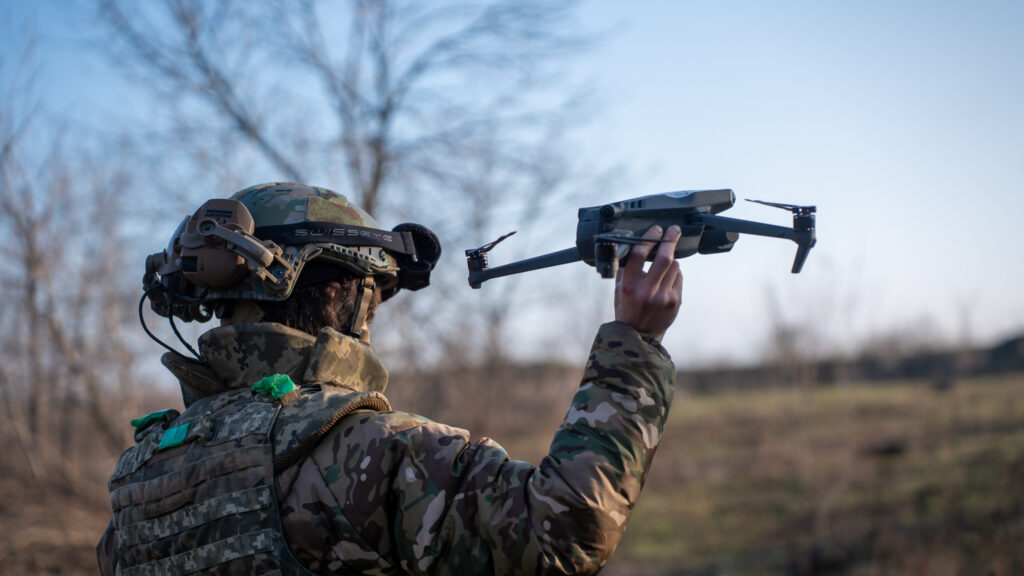 ukrainian soldier in camouflage is raising a small drone , preparing for takeoff in a forested landscape, with trees visible in the background. Soldier launches drone for reconnaissance. MyDefence
